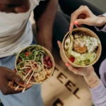 Two people holding bowls of balanced meals with vegetables, grains, and protein, representing healthy eating without pressure.